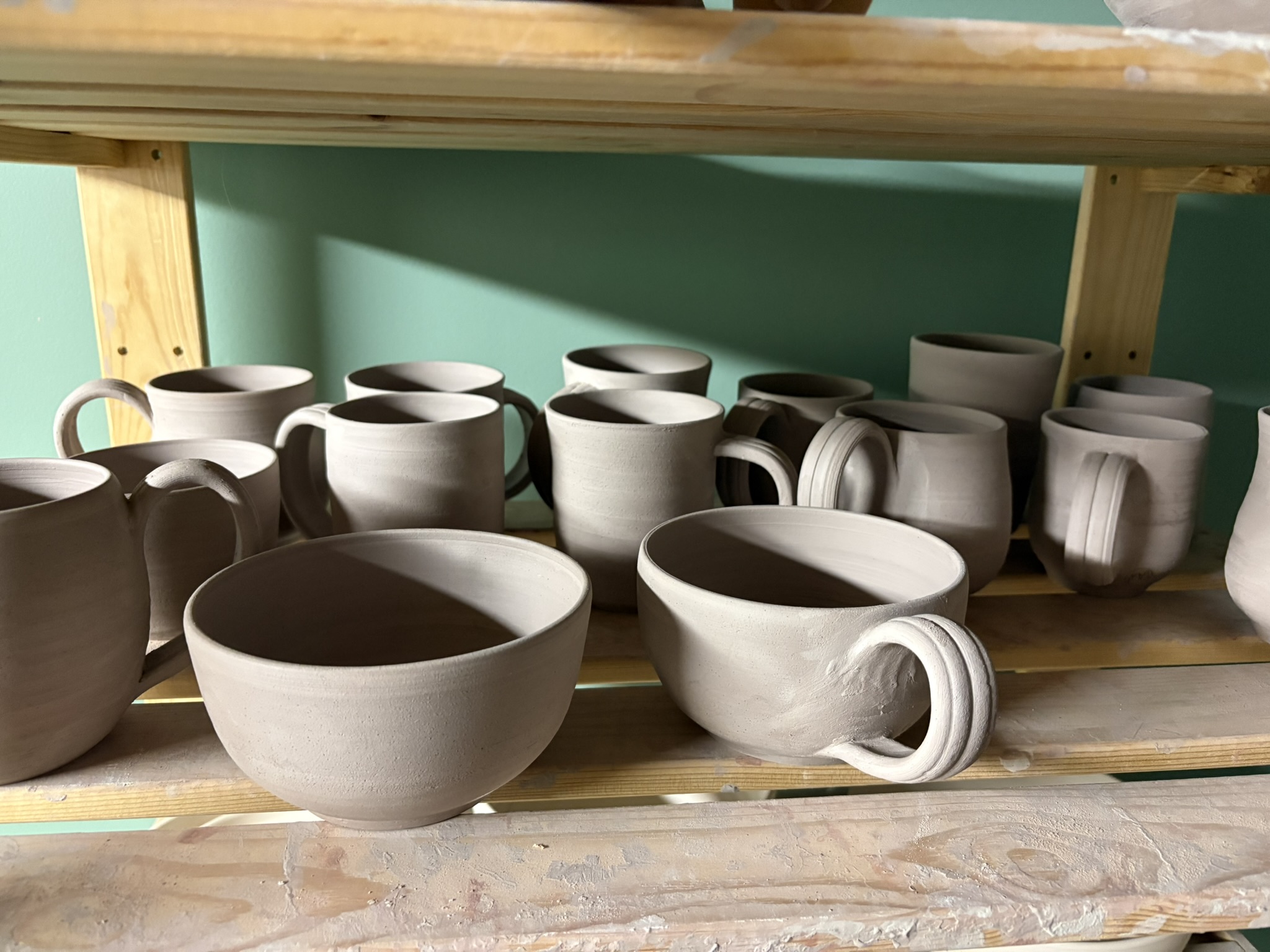 Newly made mugs and bowls drying on a studio shelf