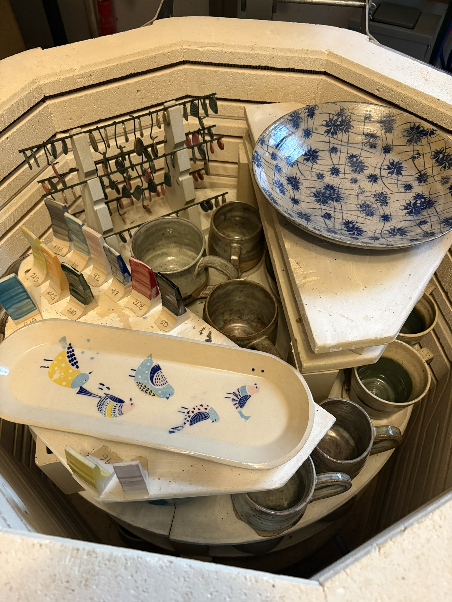 An open kiln filled with glazed mugs and bird-decorated serving dishes
