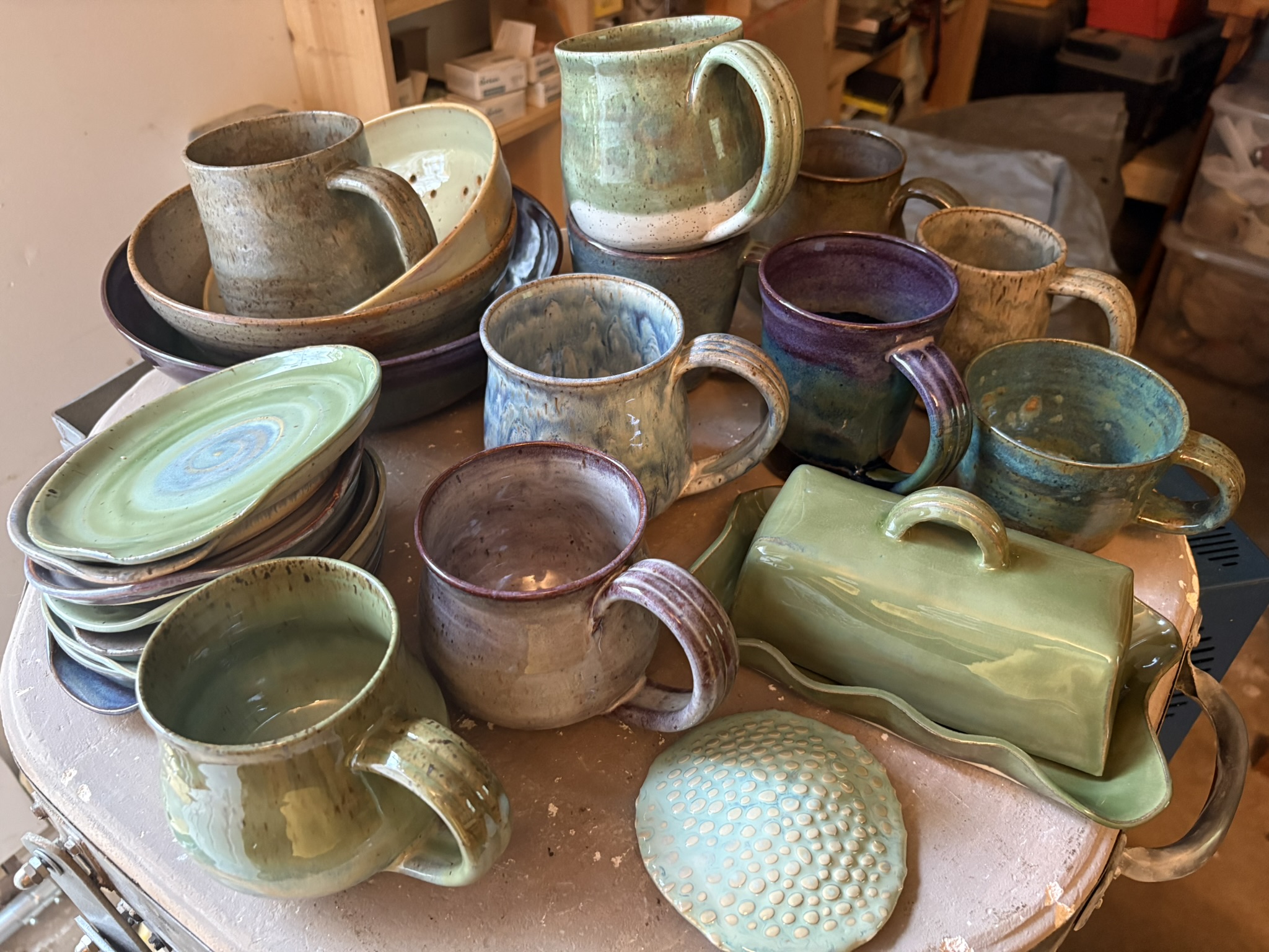 A collection of handmade mugs, small plates, and a green butter dish