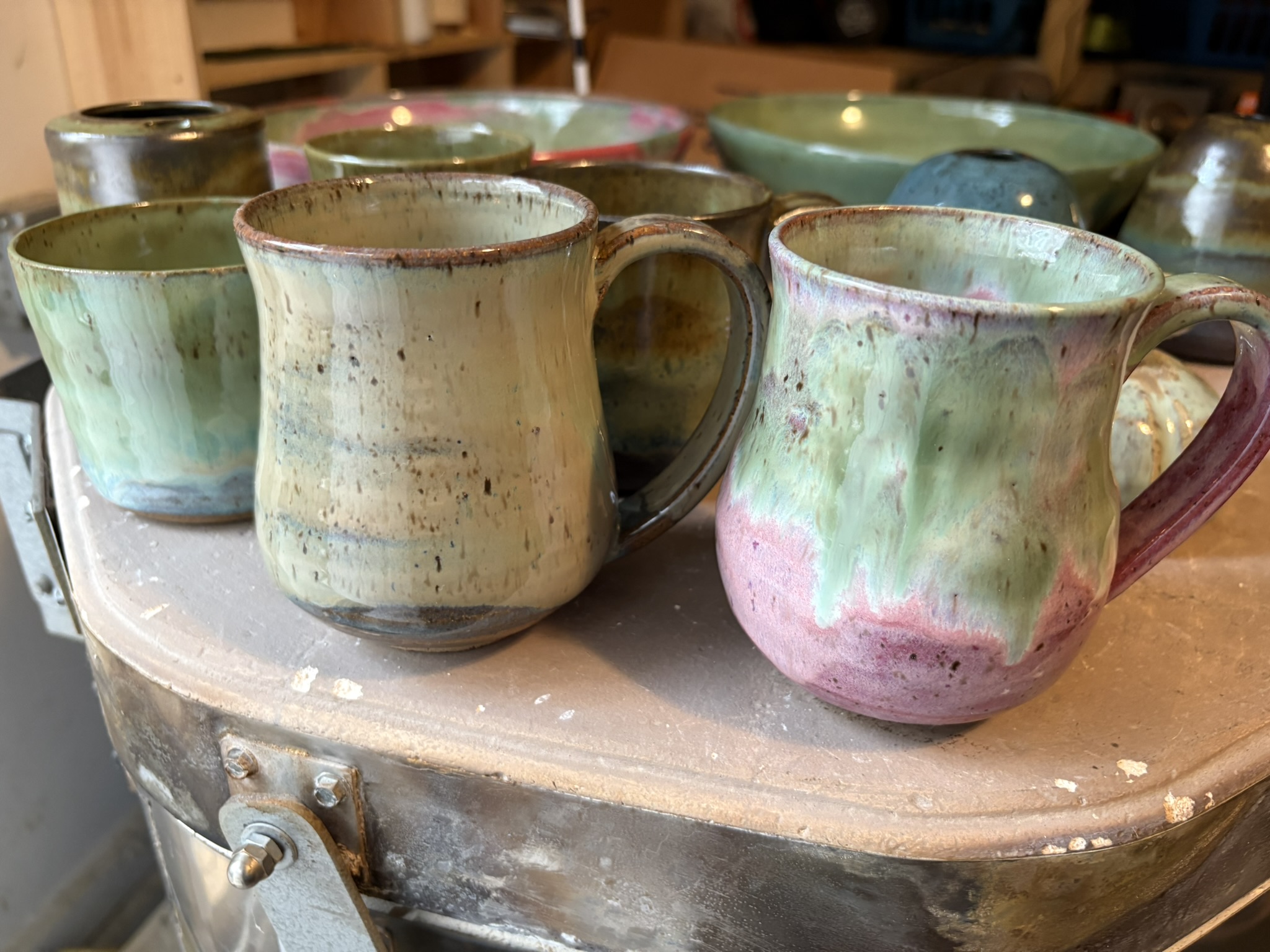 Handmade mugs in softly layered green, cream, and pink glazes