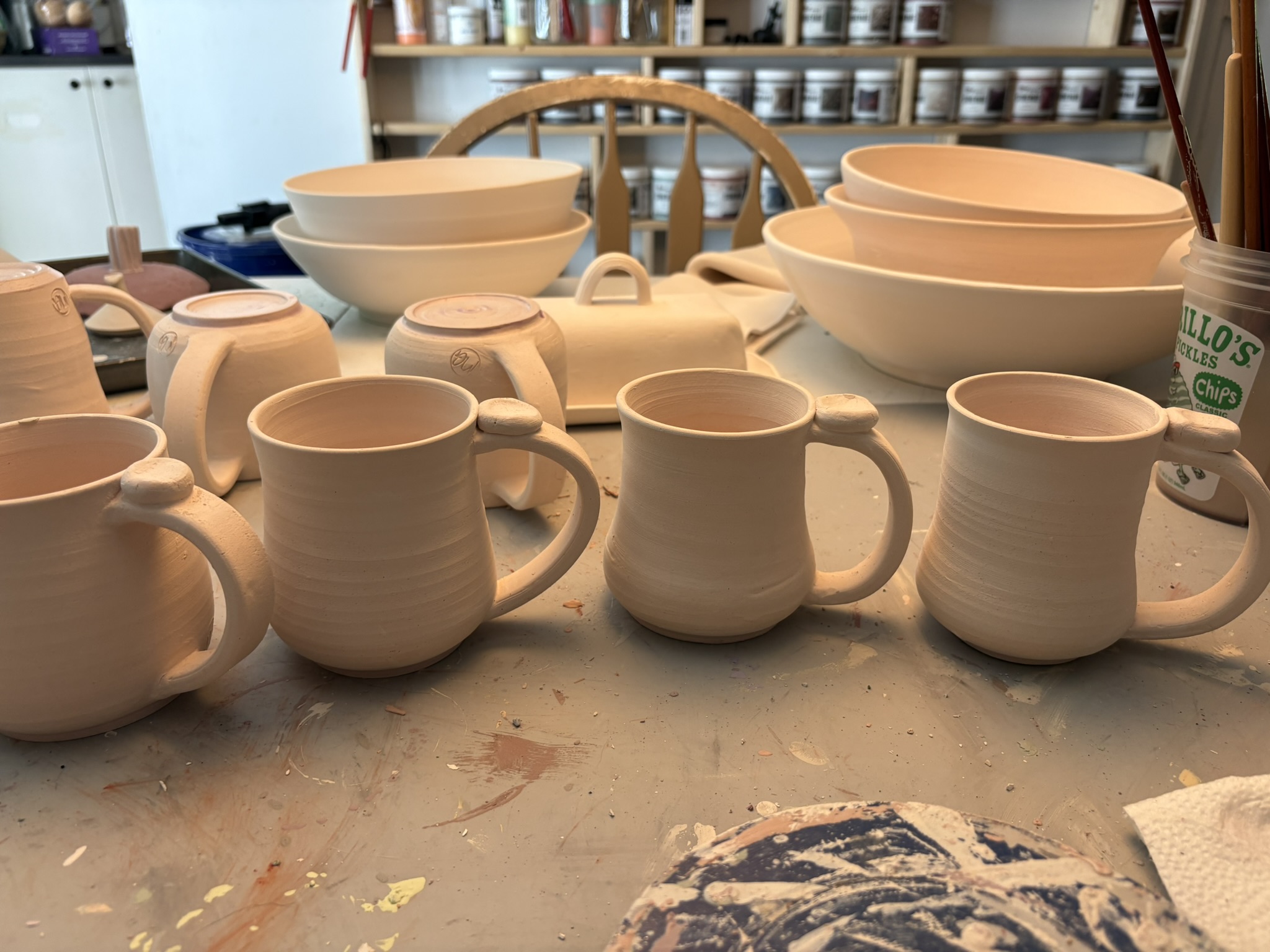 Unfired mugs, bowls, and serving pieces in the studio